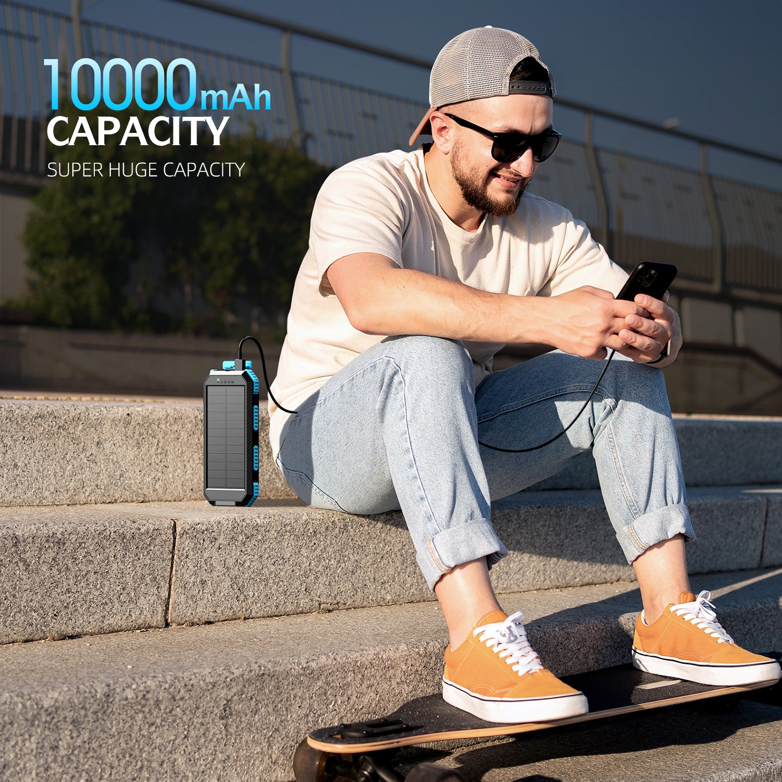 The picture shows a person sitting on stairs using a smartphone, with a 10,000mAh capacity portable power bank connected to the phone, emphasizing its large storage capacity.
